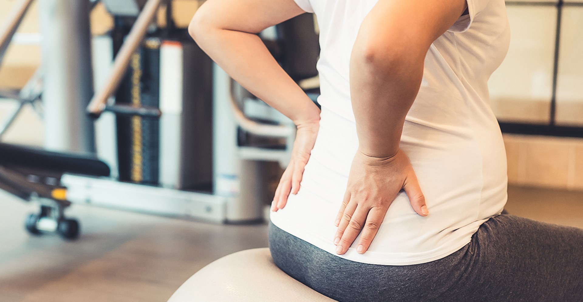 Eine Frau sitzt auf einem Gymnastikball und hält mit beiden Händen ihren Rücken fest.