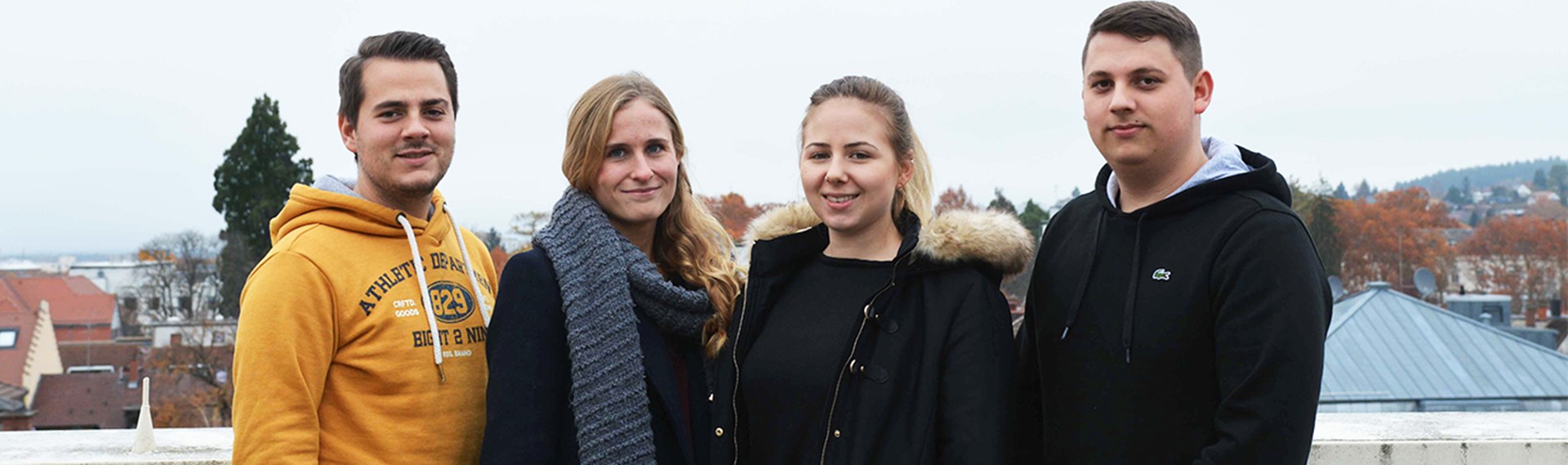 Vier junge Menschen - im Hintergrund sieht man Dächer.