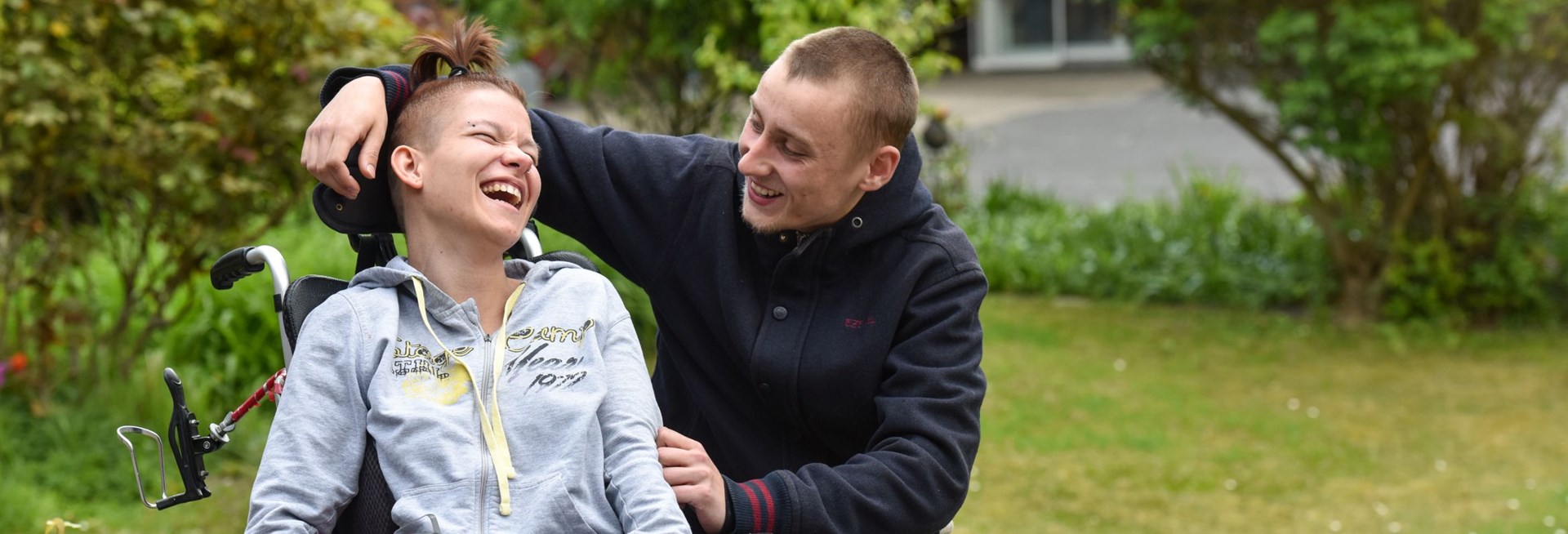 Frau mit Behinderung in Rollstuhl lachend mit Freund