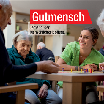 Keyvisual Gutmensch Motiv Pflege- ohne Logo Pflegerin am Tisch sitzend mit Bewohnern in Pflegeheim