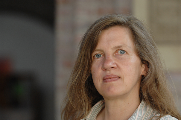 Eine Frau mit langen, welligen, dunkelbolnden Haaren schaut ernst in die Kamera.