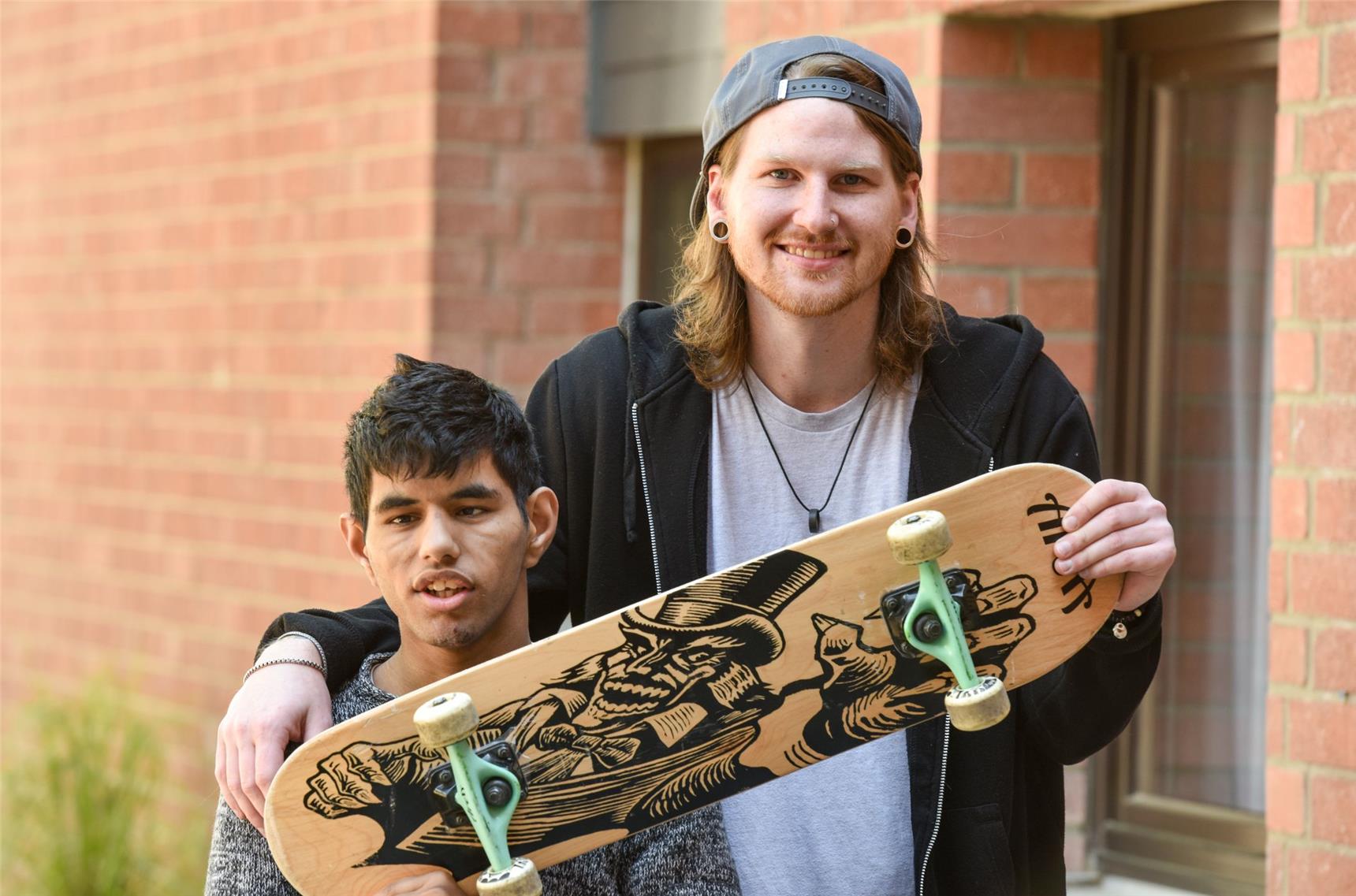 Junge mit Behinderung steht neben Freund, der seinen Arm um ihn legt