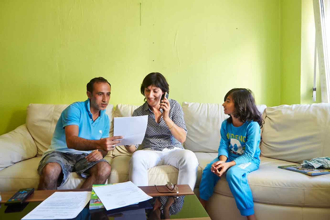 Mann, Kind und Frau sitzen am Tisch, die Frau telefoniert.
