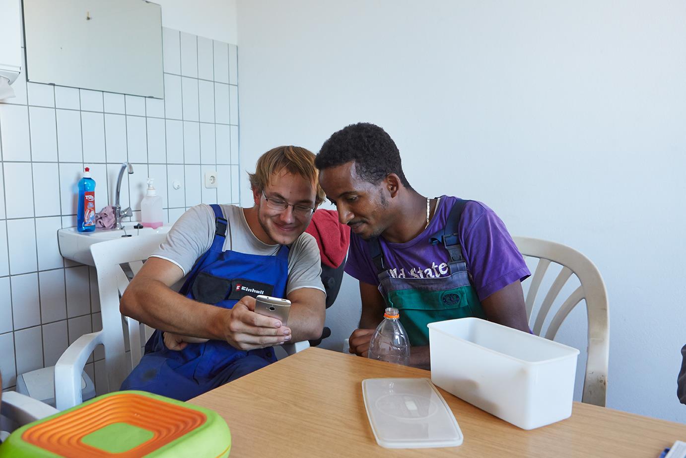 Zwei Männer in Bauarbeiterkluft schauen gut gelaunt auf ein Handy