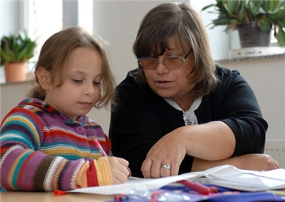 Ehrenamtliche Hausaufgabenhilfe Frau hilft Mädchen bei Schulaufgaben