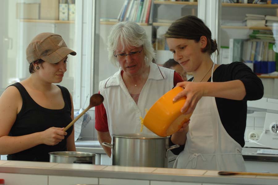 Zwei Jugendliche mit einer Frau beim Kochen.