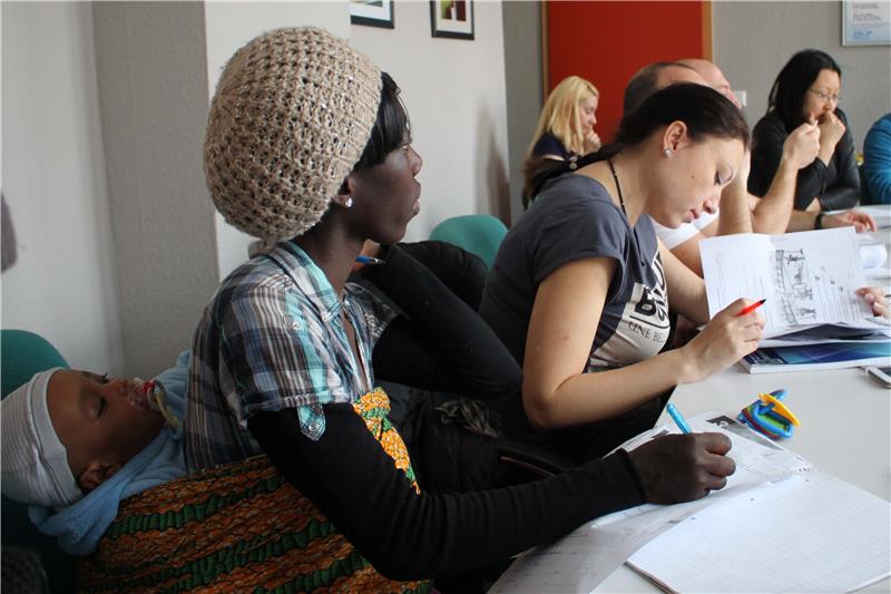 Eine Mutter mit ihrem Baby auf dem Rücken gebunden sitzt im Deutschkurs