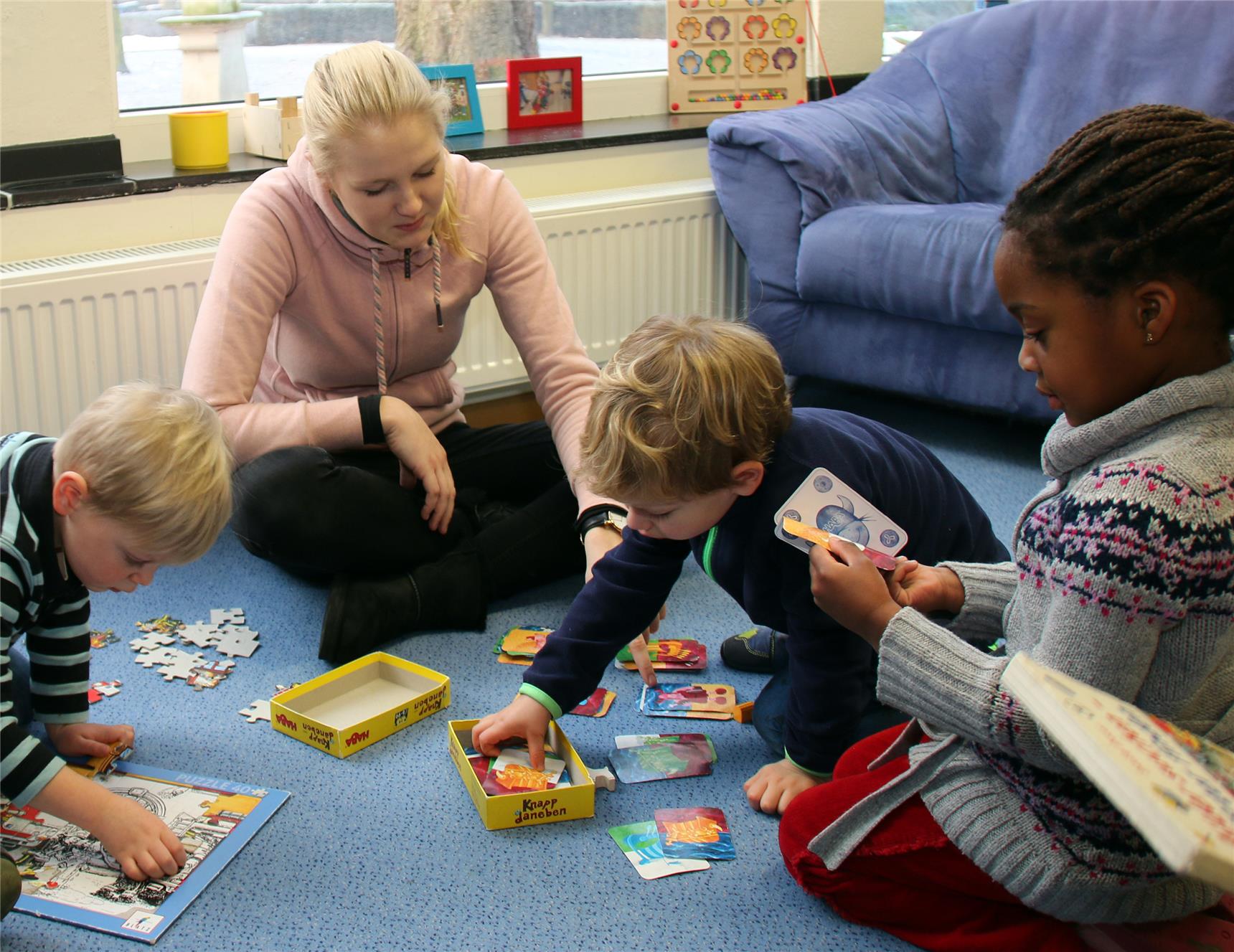 Drei Kinder und eine Frau sitzen auf einem Teppich und spielen.