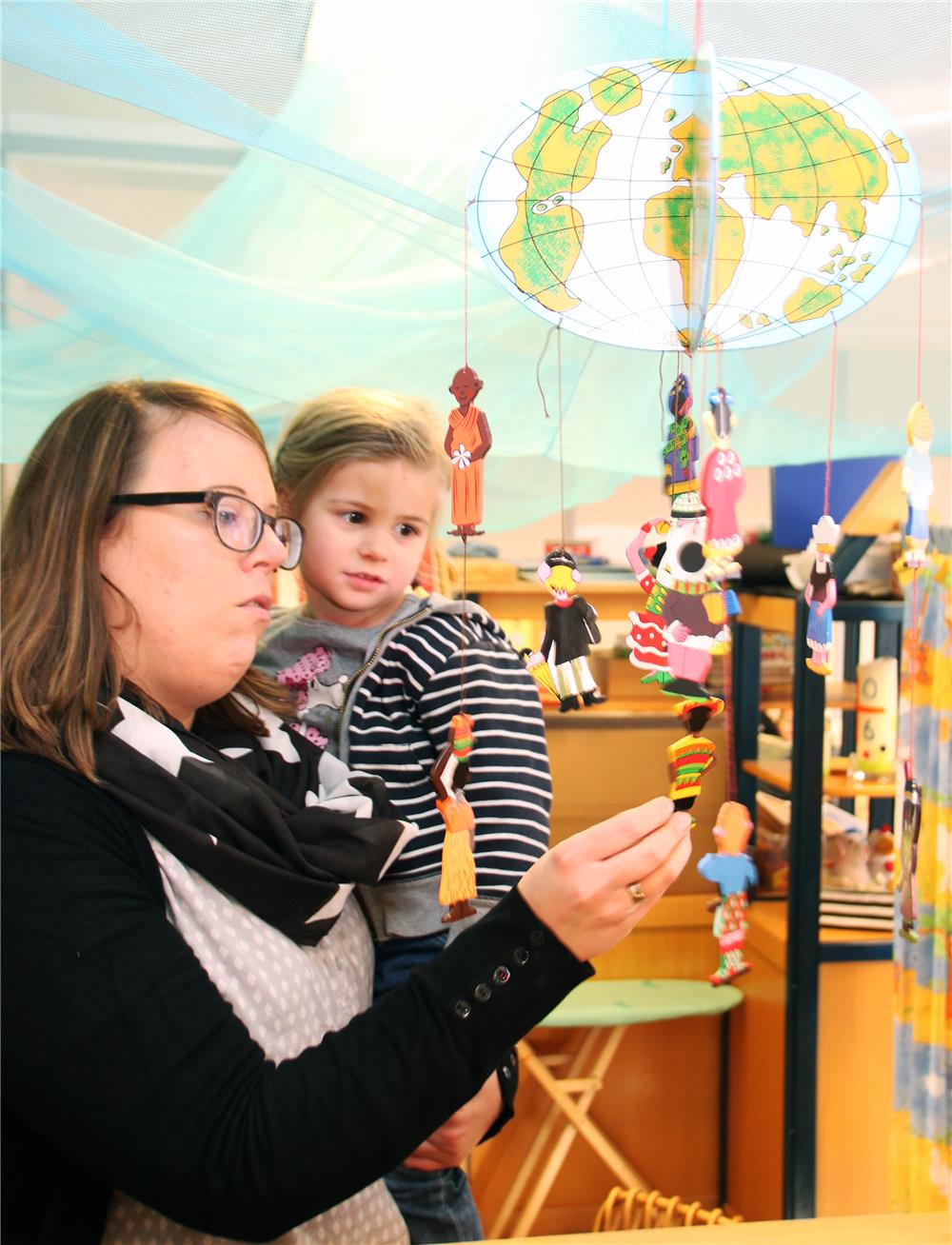 Eine Frau hat ein Mädchen auf dem Arm und zeigt ihr ein Mobile.