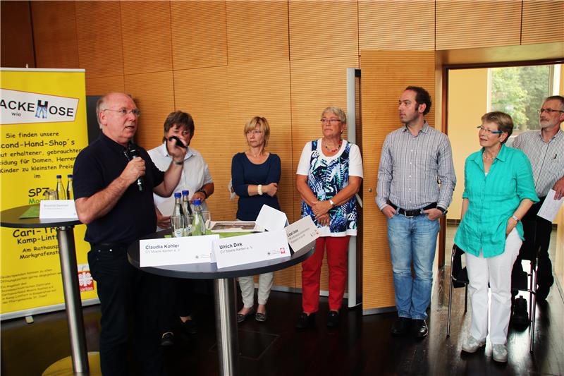 Das Foto zeigt eine Gruppe von Menschen nebeneinander stehend, einer spricht in ein Mikrofon.