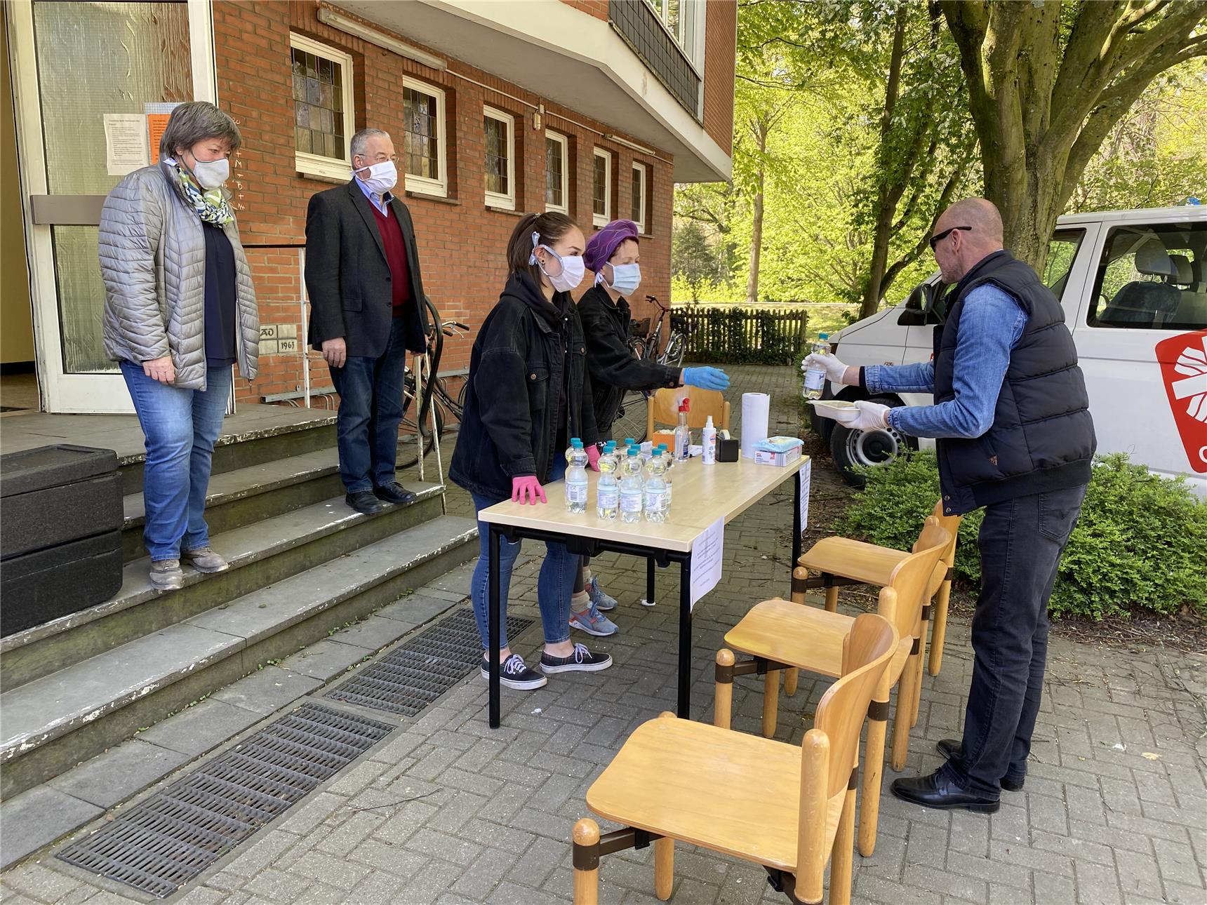 Das Foto zeigt zwei Ehrenamtliche, die an einem Tisch Essen an einen Mann übergeben.
