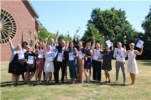 060-2022_Abschluss Leitungskurs Im Freien auf einer grünen Wiese stehen 17 Kursteilnehmer*innen mit Zertifikatmappen und Rosen, die sie in die Luft strecken