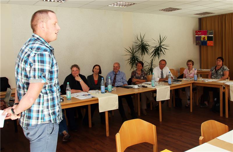 Das Foto zeigt einen Redner vor einigen Zuhörern, die an einem Tisch sitzen.