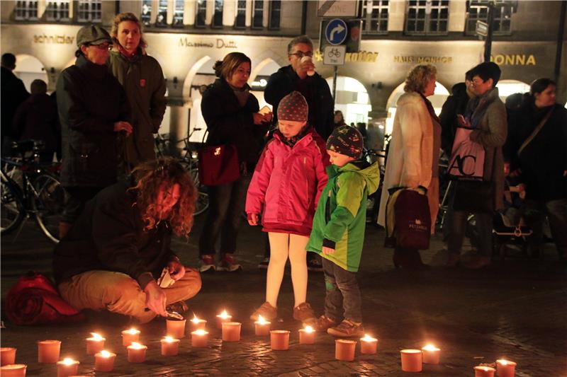 Das Foto zeigt Kinder und Erwachsenen, die vor ihnen aufgestellte Kerzen betrachten, ein Mann sitzt auf dem Boden und zündet eine Kerze an.