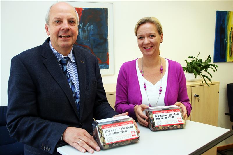 Ein Mann und eine Frau stehen nebeneinander an einem Tisch in einem Raum. Auf dem Tisch liegen zwei Dosen, die mit Kleingeld gefüllt sind.