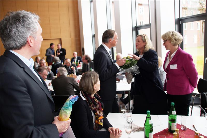 Das Foto zeigt zwei Frauen, die einem Mann Blumen überreichen im Rahmen einer Versammlung.