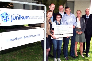 057-2015 Stiftungsspende Das Foto zeigt eine Gruppe von Menschen neben einem großen Schild mit dem Namen der Einrichtung Junikum