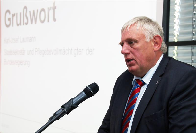 Das Foto zeigt einen Redner vor einem Mikrofon, im Hintergrund eine Leinwand.