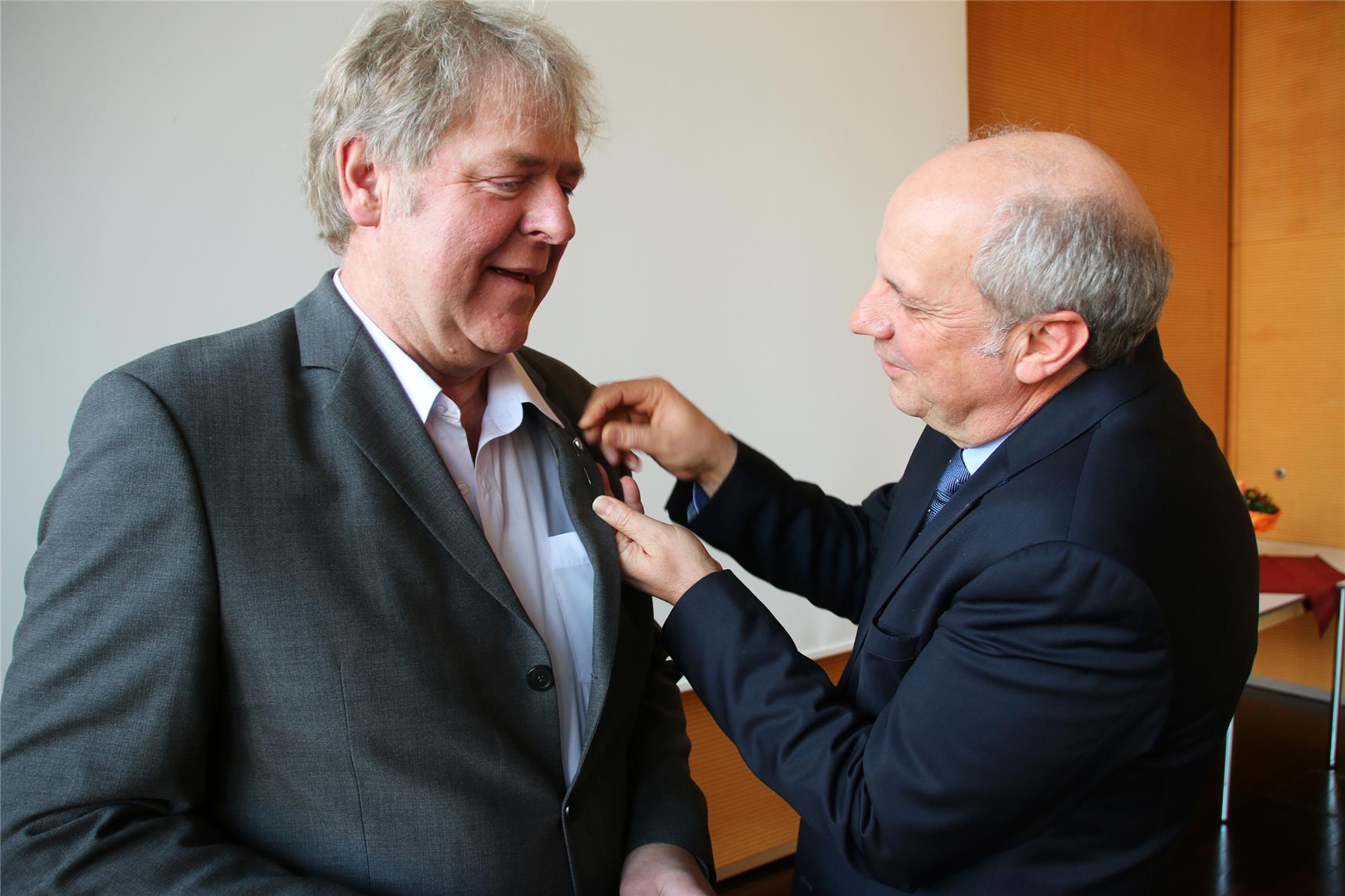 Ein Mann heftet eine Ehrennadel an das Revers eines anderen Mannes