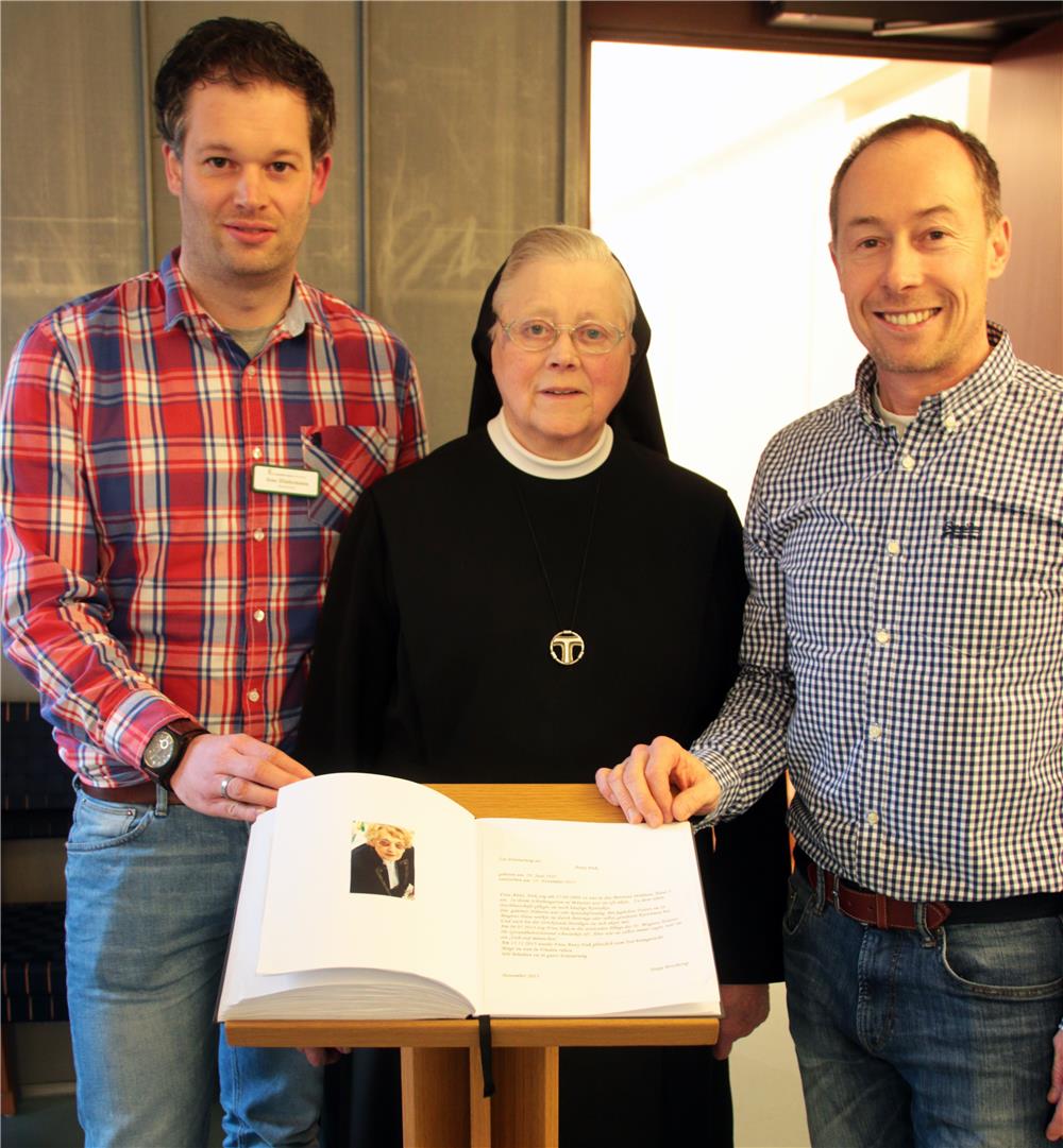 Drei Personen stehen vor einem Gedenkbuch.