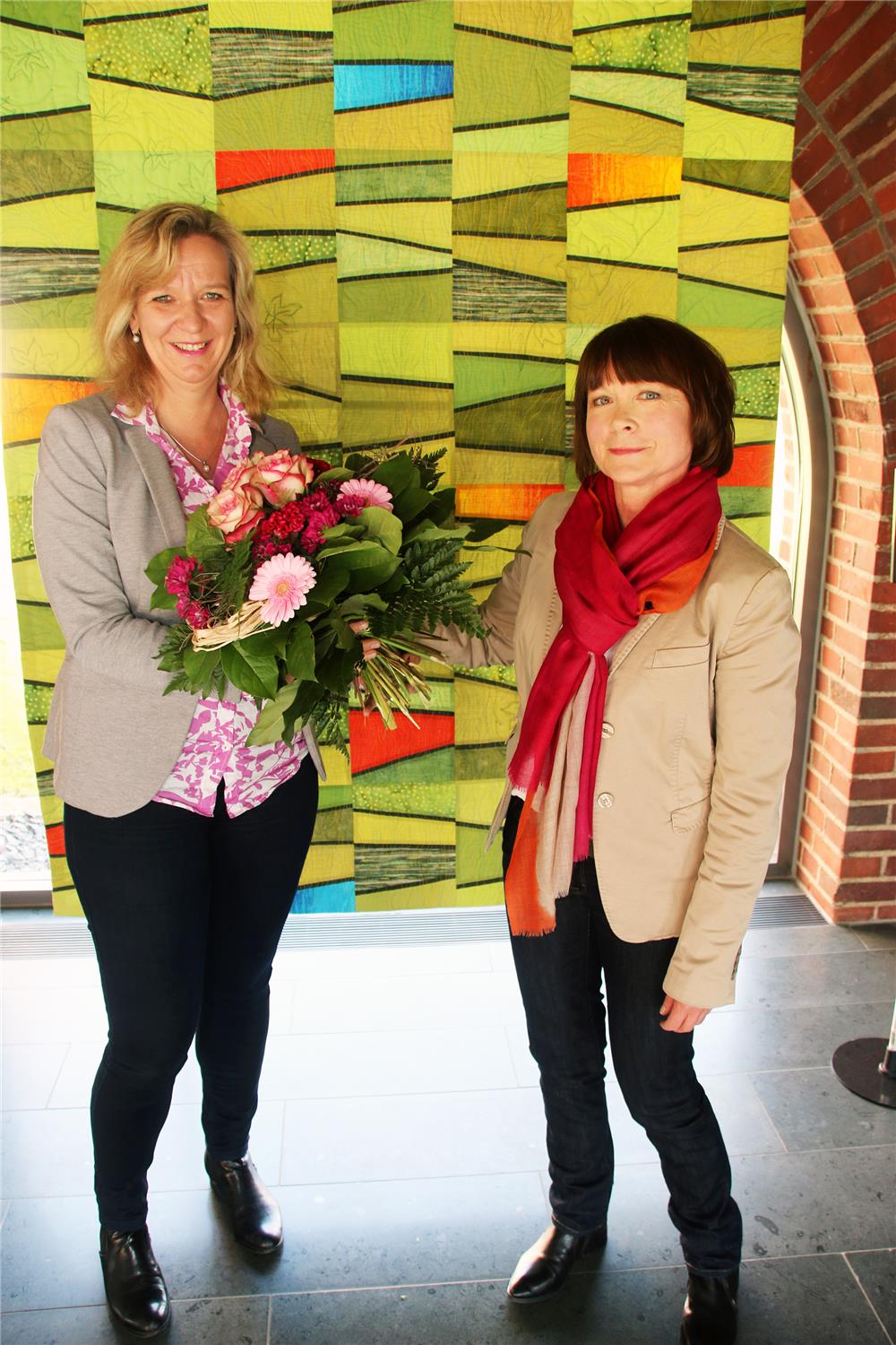 Zwei Frauen stehen vor einem farbenfrohen Quilt.