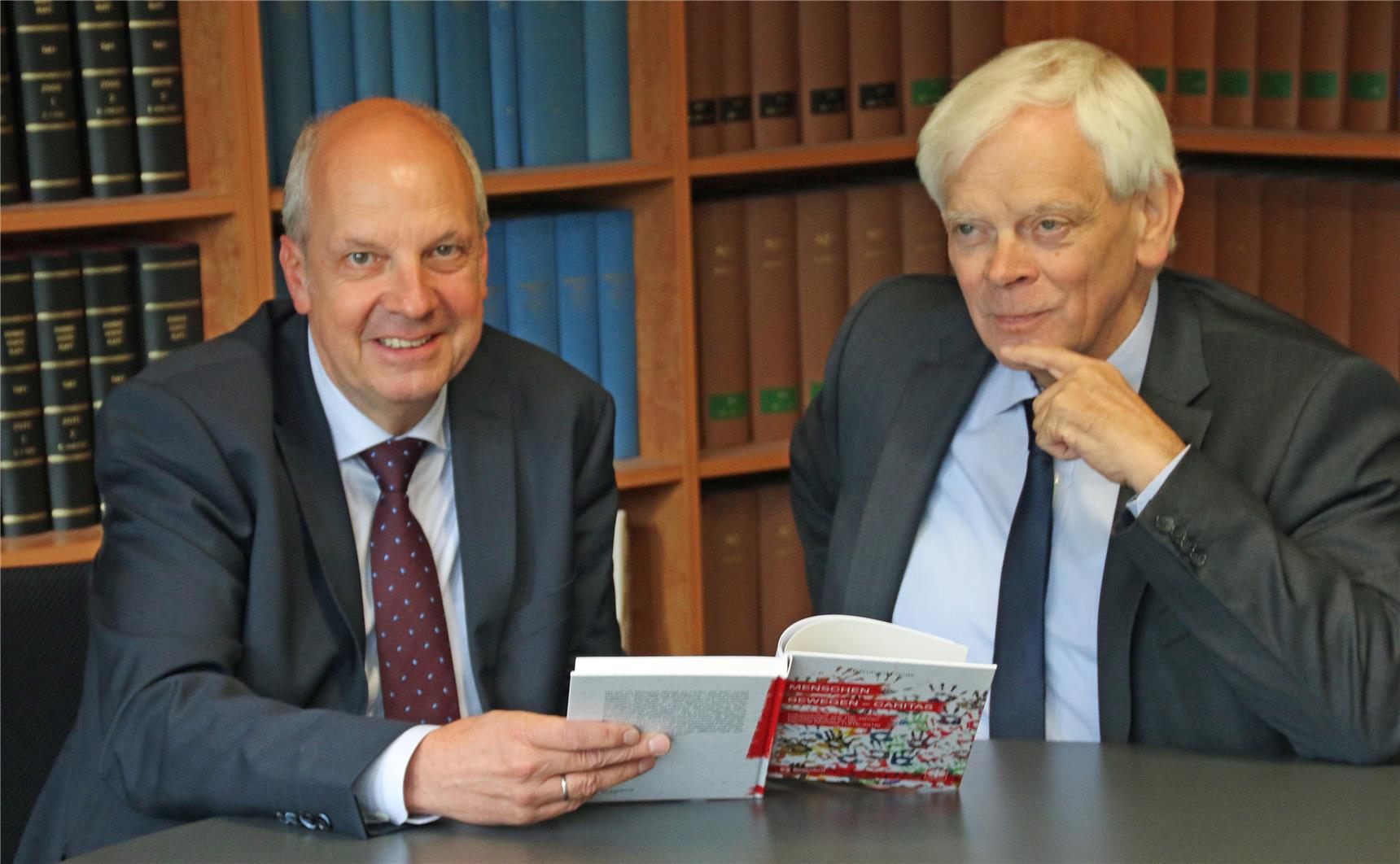 Das Foto zeigt zwei Männer, die ein Buch präsentieren, vor einer Bücherwand.