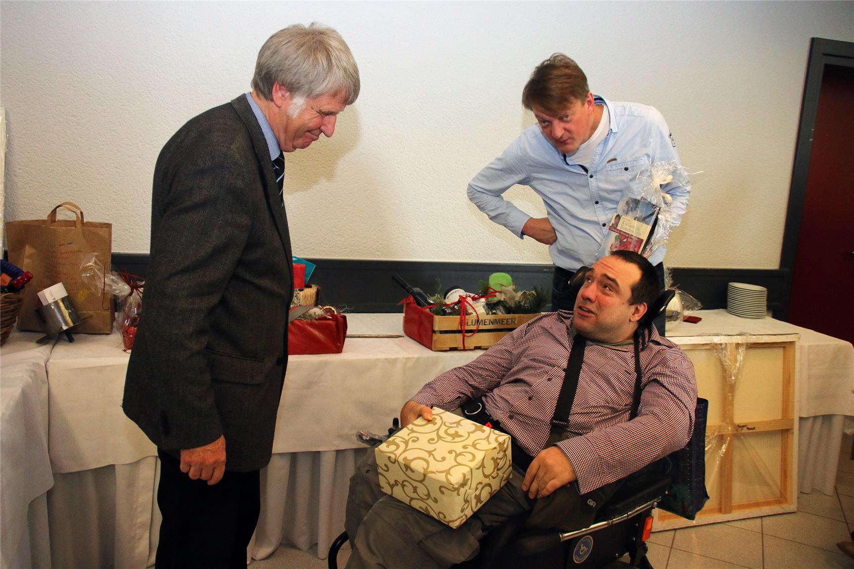 Auf dem Bild sitzt ein Mann im Rollstuhl, zwei andere stehen