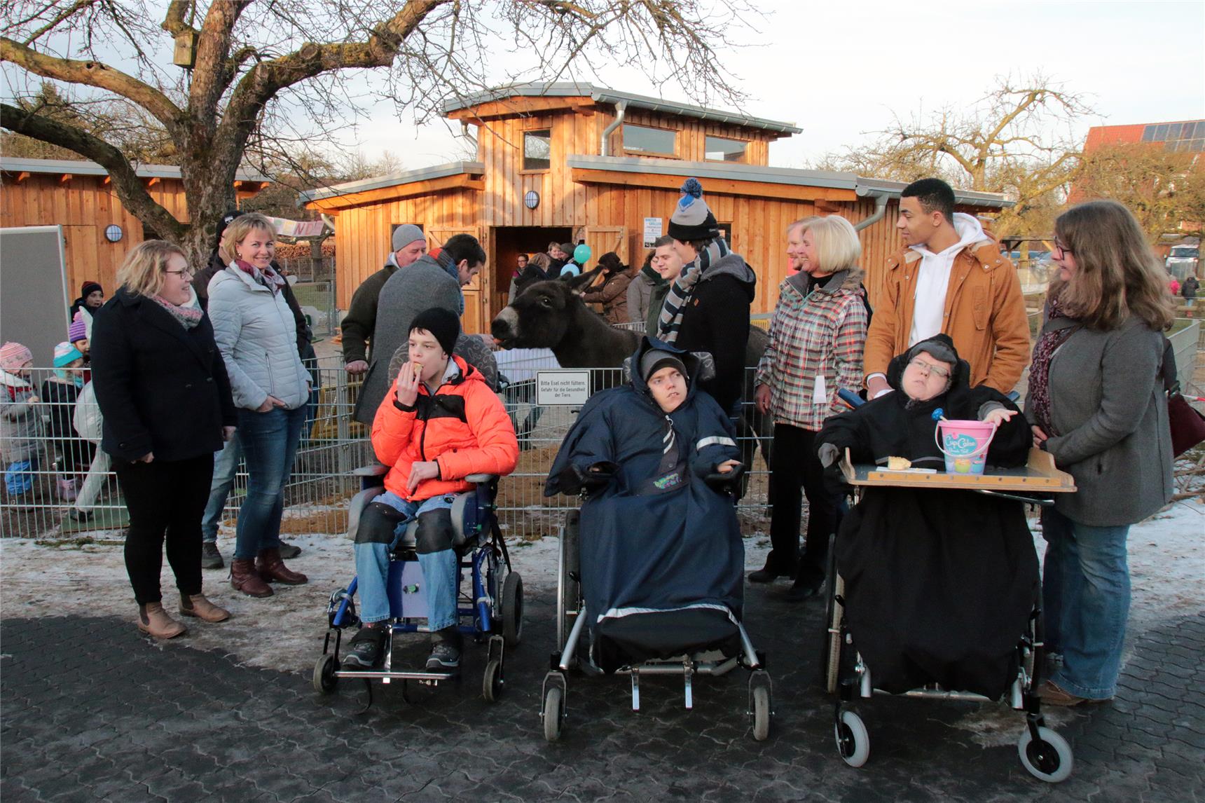 Das Foto zeigt eine Gruppe von Menschen vor einem Stall, ein Esel wird gestreichelt.