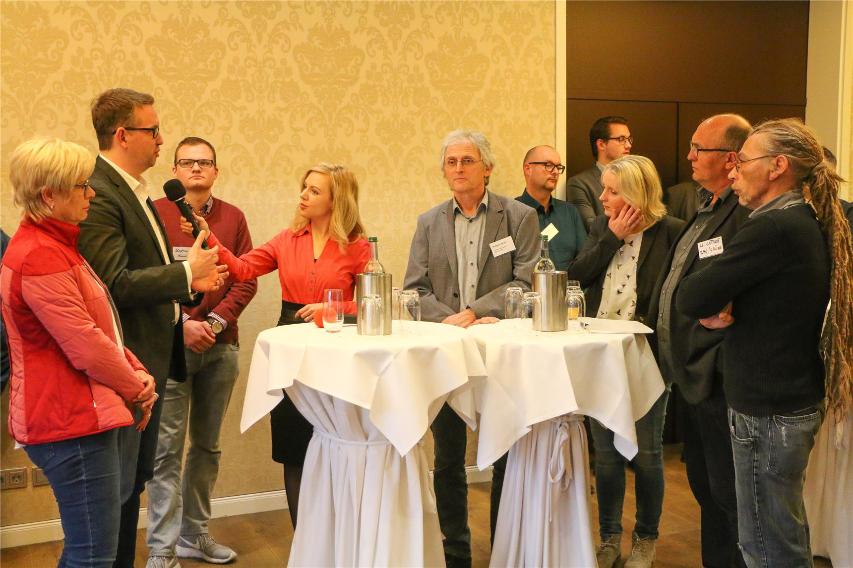 Einige Menschen stehen am Stehtisch und unterhalten sich mit der Moderatorin.