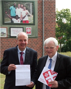 040-2017_Caritas2025_Start Das Foto zeigt zwei Männer mit Broschüren vor einem großen Gebäude.