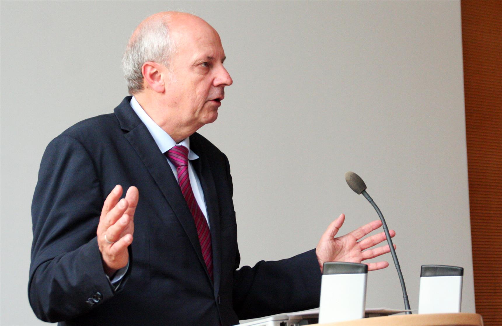 Das Foto zeigt einen Redner an einem Pult vor einem weißen Hintergrund.