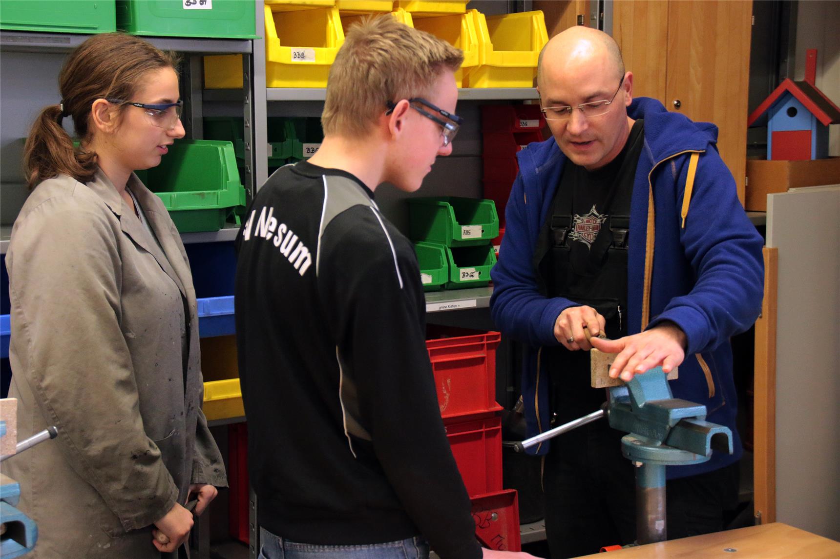 Der Ausbilder steht mit zwei Auszubildenden im Werkraum und feilt.