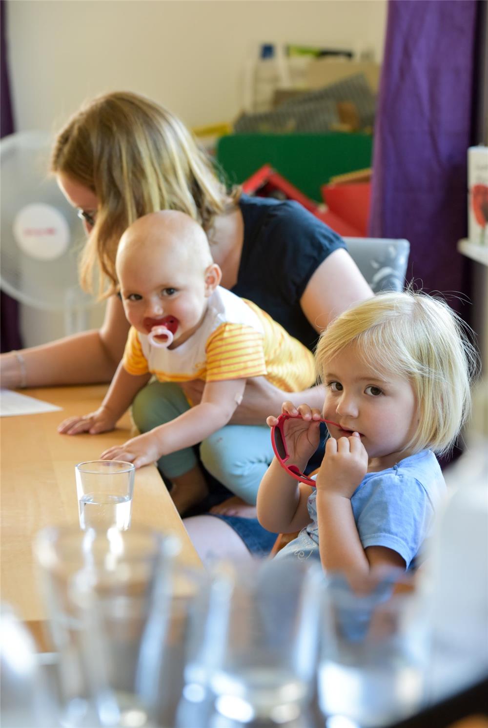 Das Foto zeigt eine Mutter mit zwei Kindern an einem Tisch, die schreibt.