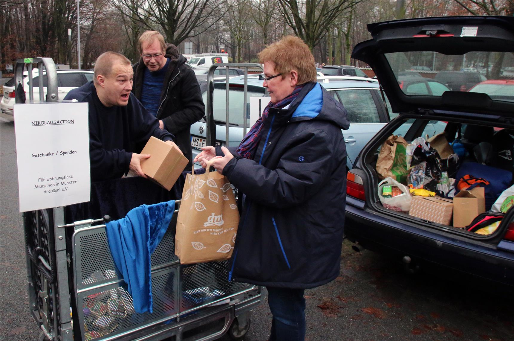Das Foto zeigt drei Menschen, die aus einem Wagen verschiedene Materialien in ein Auto umladen.