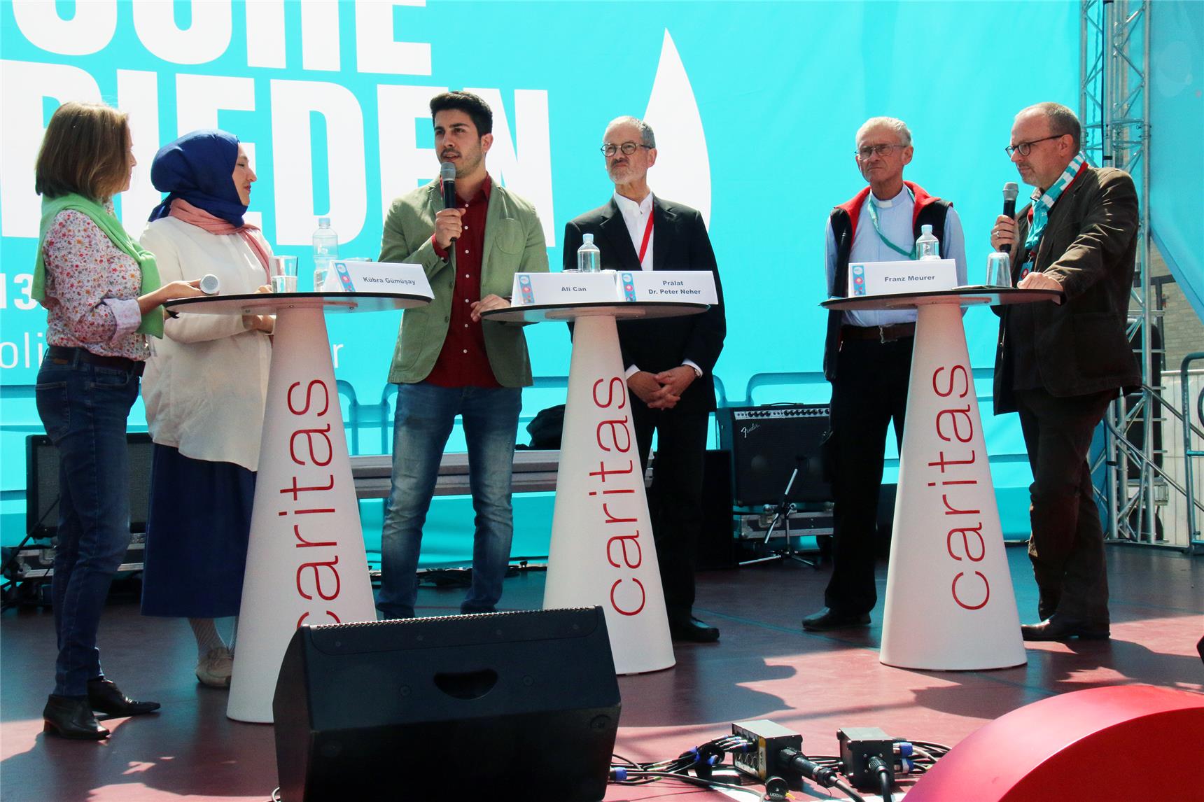 Das Foto zeigt sechs Menschen auf einer Bühne an Stehtischen.