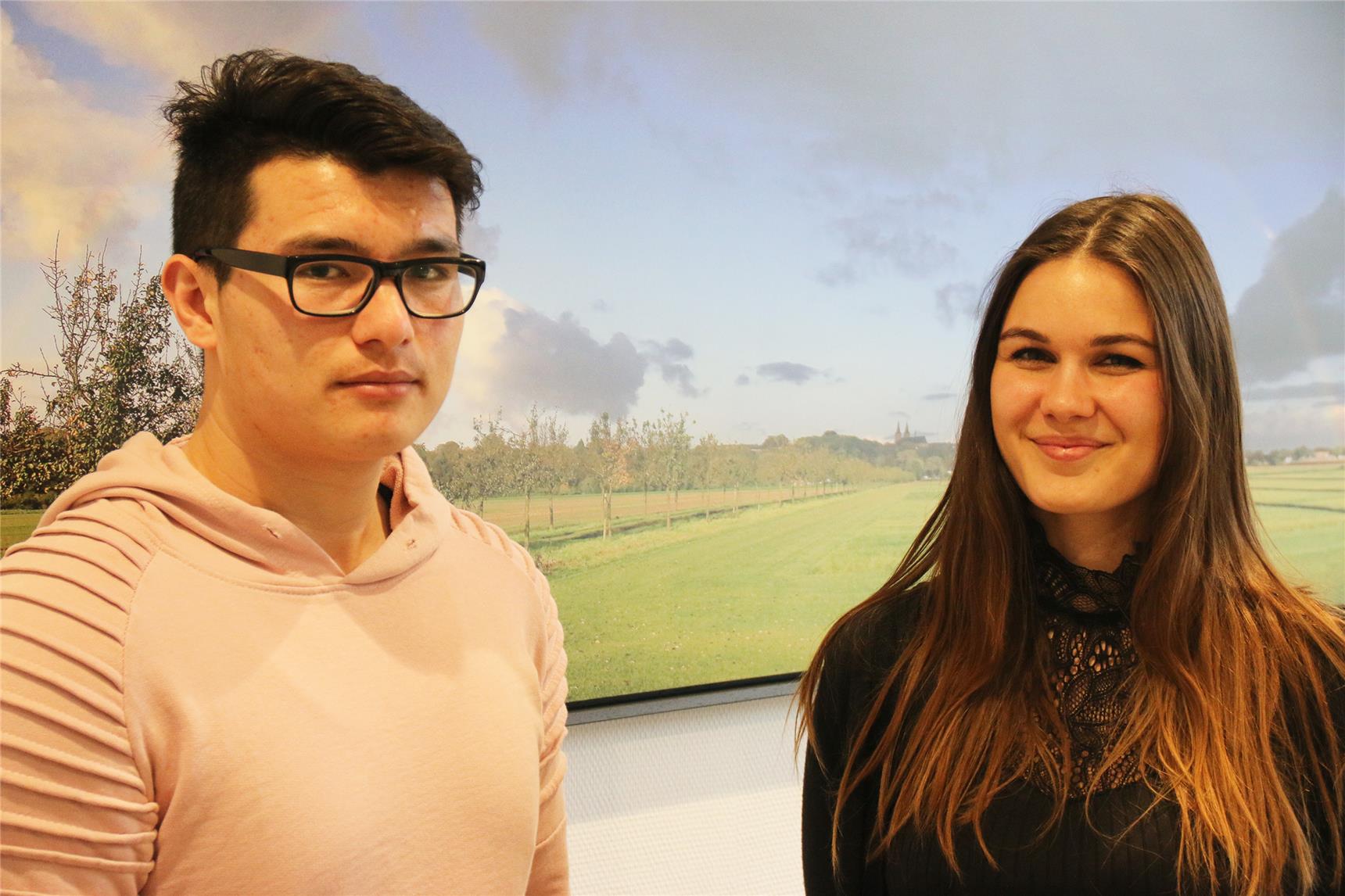 Das Foto zeigt einen jungen Mann und eine junge Frau, die vor einem großen Landschaftsbild stehen.
