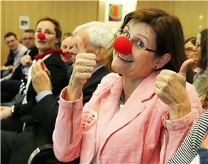 0037-2019_Altenhilfekongress Das Foto zeigt eine Frau, die eine rote Nase aufhat und begeistert in die Kamera schaut.
