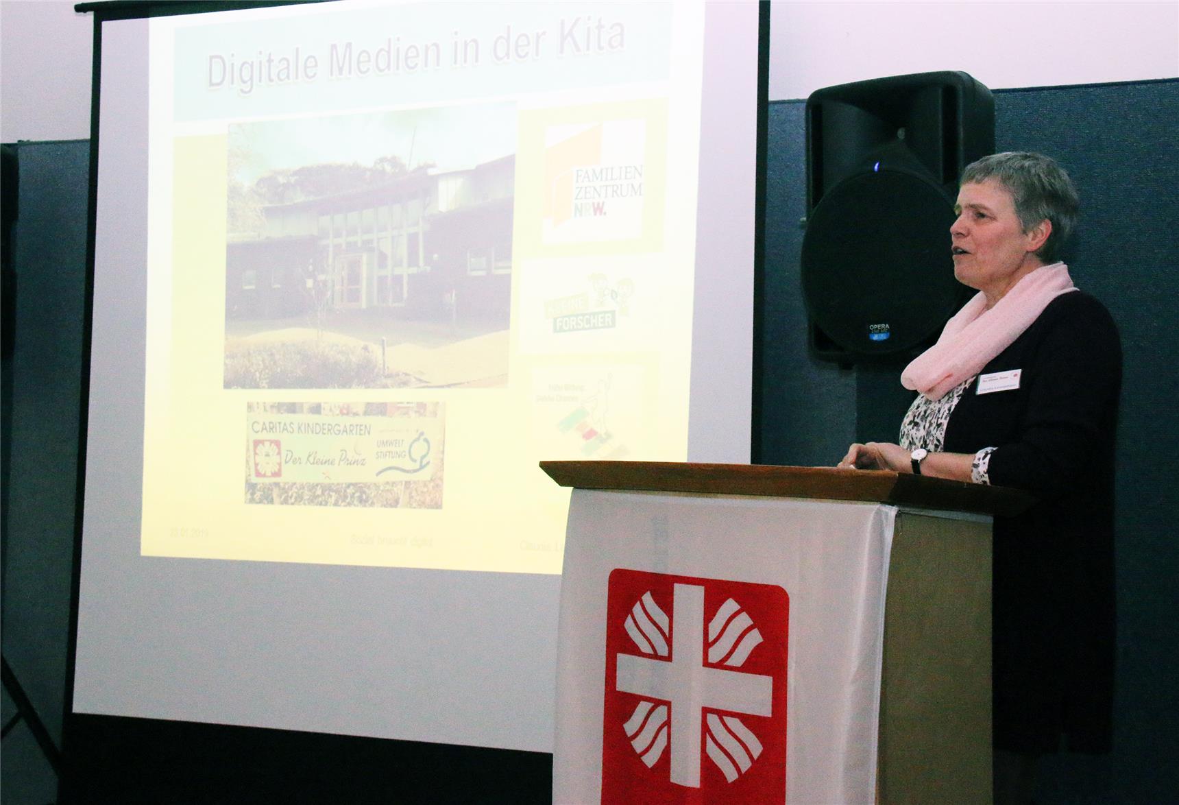Das Foto zeigt eine Frau an einem Rednerpult und daneben eine Projektion auf einer Leinwand-