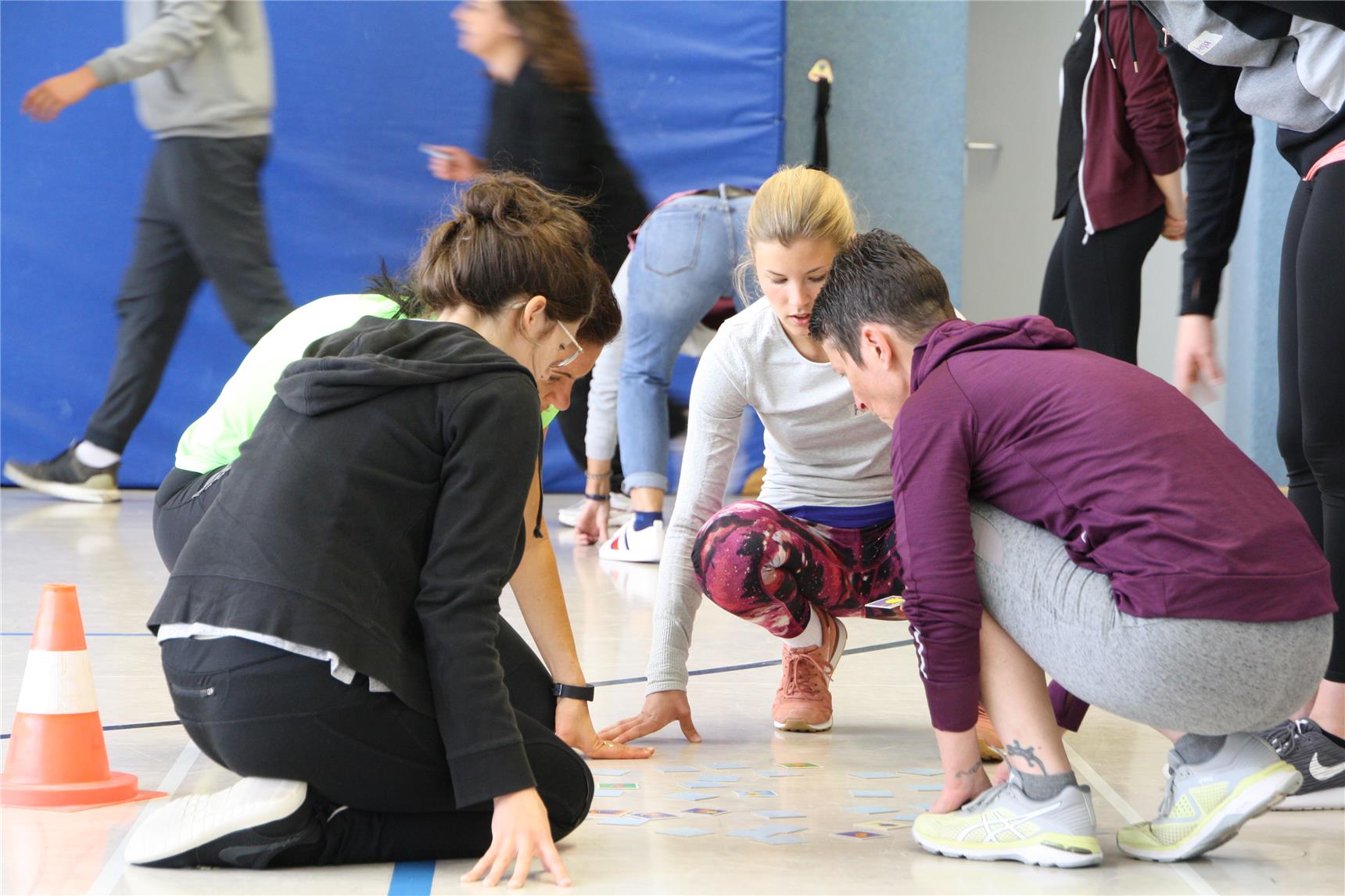 Vier Personen hocken in einer Turnhalle und schauen sich etwas auf dem Boden an.