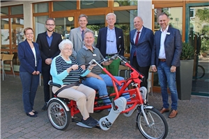 059-2019_Mobil im Alter Eine 83jährige Bewohnerin des Edith-Stein-Hauses sitzt auf dem roten dreirädrigen Tandem. Stifter und Caritasmitarbeiter stehen daneben.
