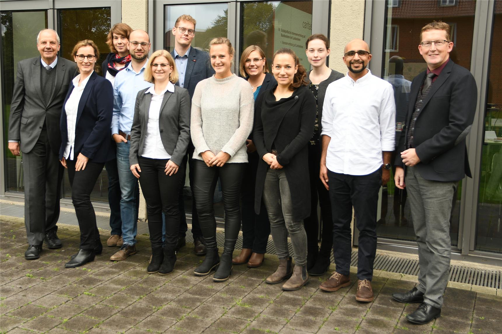 Eine Menschengruppe steht in zwei Reihen und schaut in die Kamera.