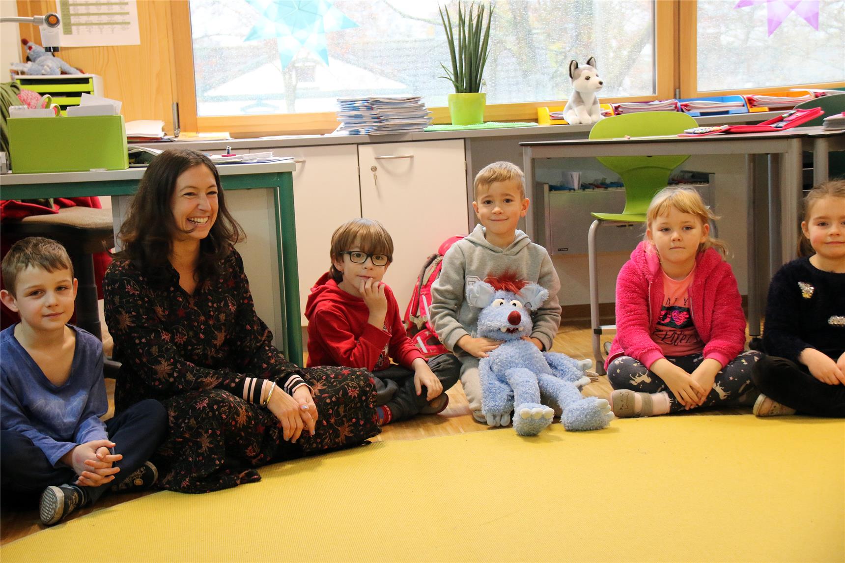 Das Foto zeigt eine Lehrerin mit Grundschulkindern, die in einem Kreis sitzen