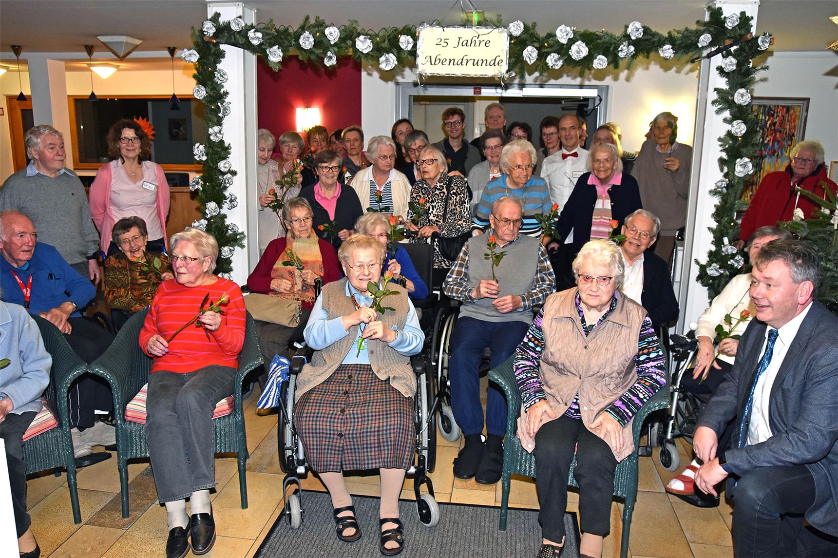 Eine große Gruppe älterer Menschen sitzen und stehen fröhlich zusammen. 