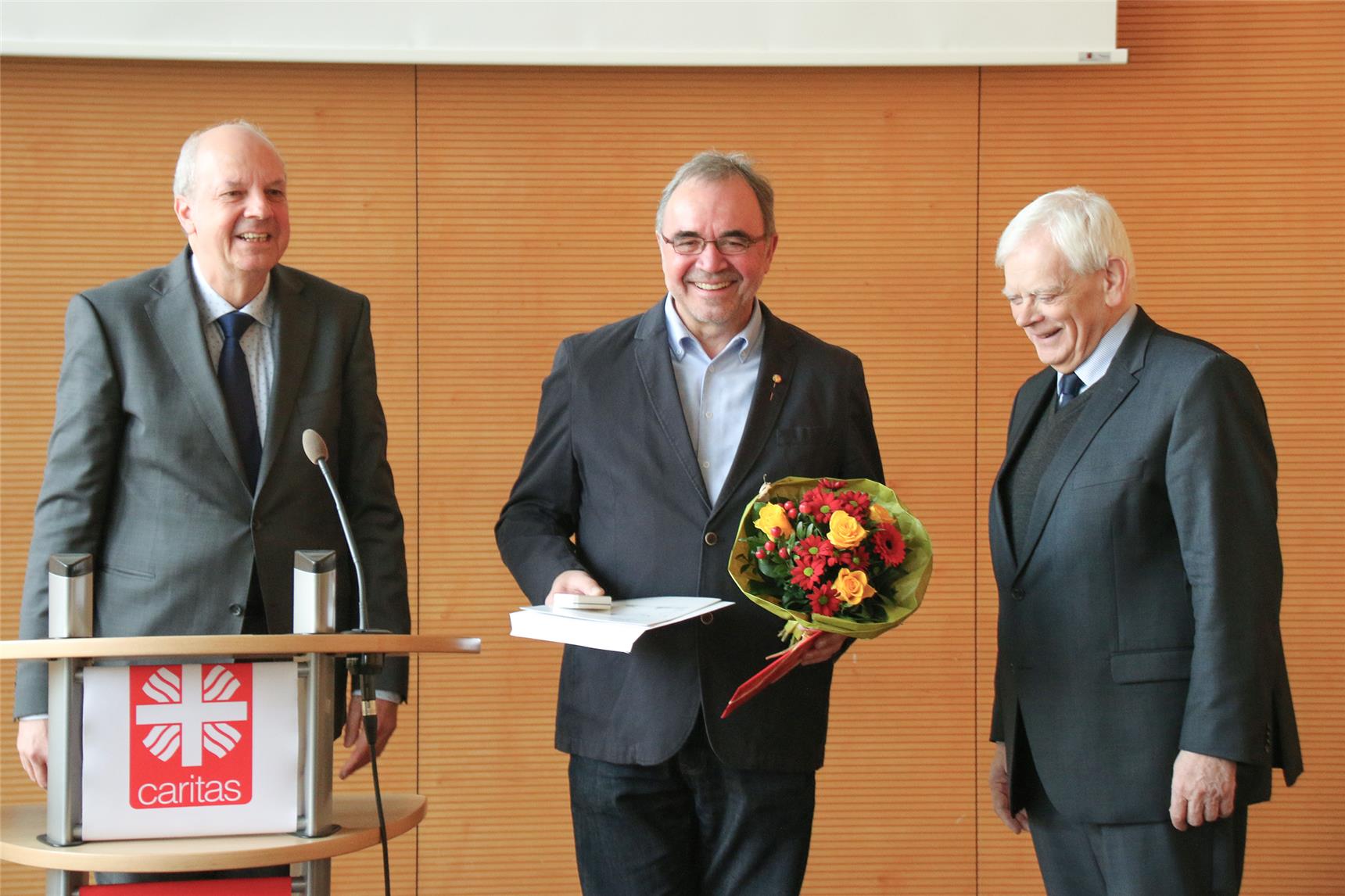 Auf dem Foto stehen drei Herren vor dem Publikum