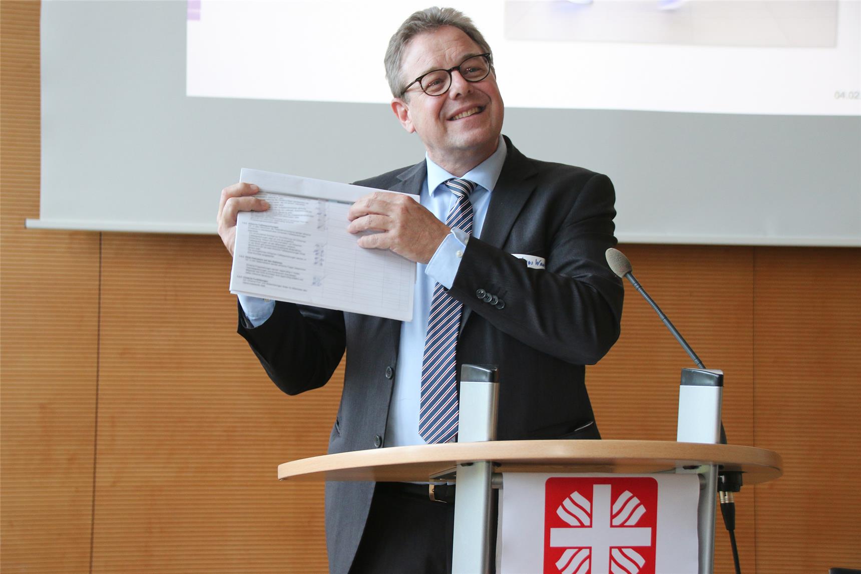 Das Foto zeigt einen Redner am Pult. der ein Papier in die Höhe hält.