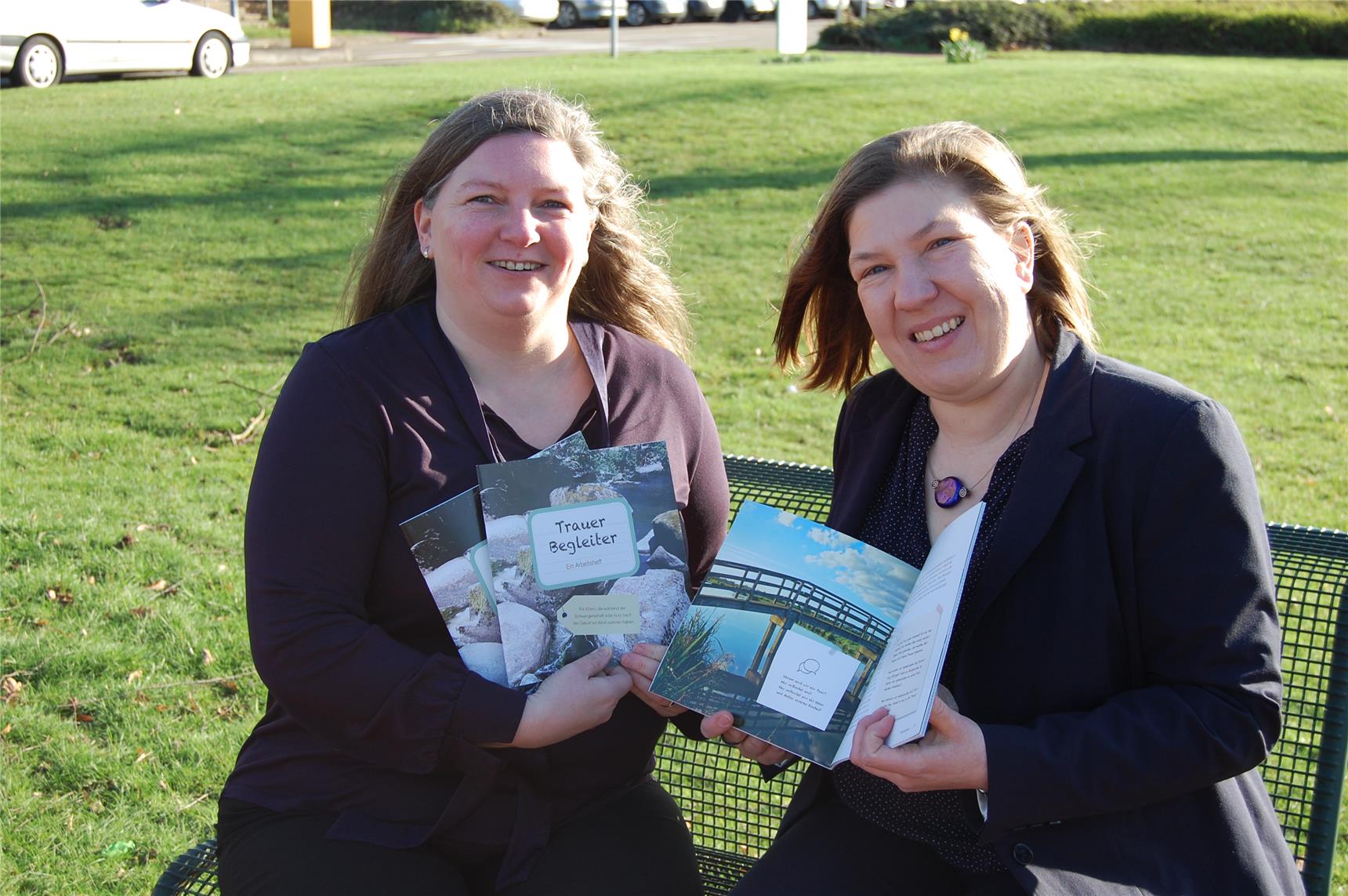 Das Foto zeigt zwei Frauen, die eine Broschüre in die Kamera halten.