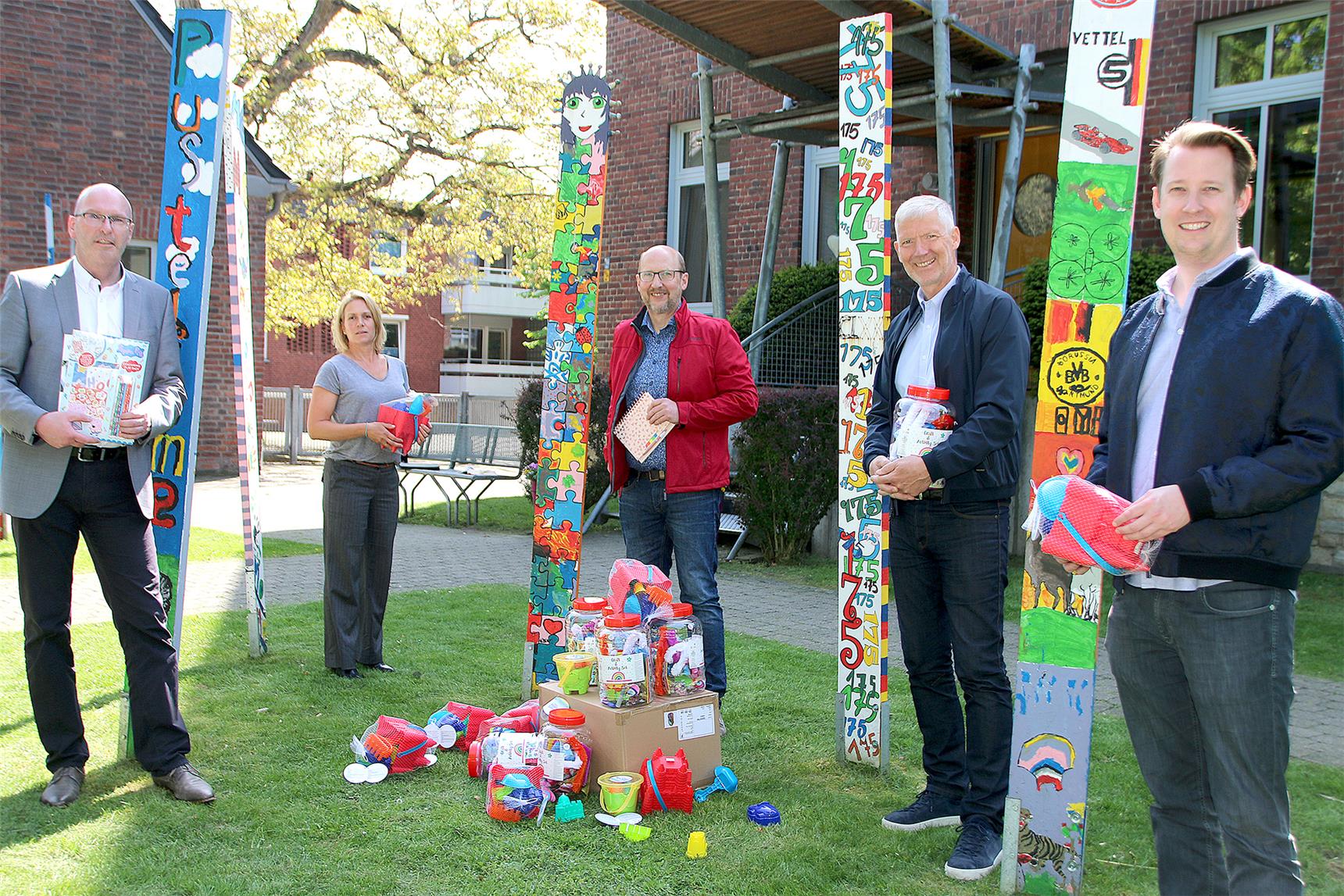 Vor dem Gebäude der Kinder- und Jugendhilfeeinrichtung St. Mauritz stehen bunte Pfähle. Zwischen ihnen verteilt stehen fünf Personen.
