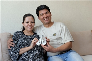 066-2020_Neuvisierung Das Foto zeigt ein junges Paar mit Migrationshintergrund, das Babyschuhe in die Kamera hält.