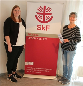 069-2020 Wohnprojekt Ibbenbüren Zwei Frauen stehen neben einem Roll-up, welches das Logo des Sozialdienst katholischer Frauen zeigt.