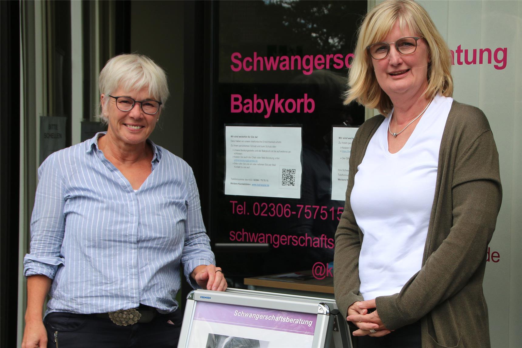 Zwei Frauen stehen vor einer Glastür, an der ein QR-Code hängt